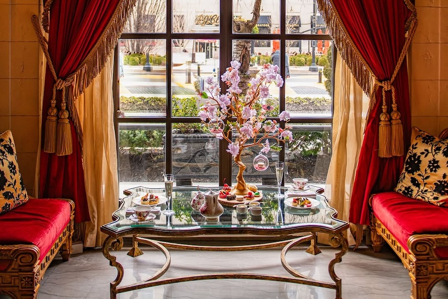 An elaborate high tea seat up with cherry blossom accents in front of red velvet curtain.