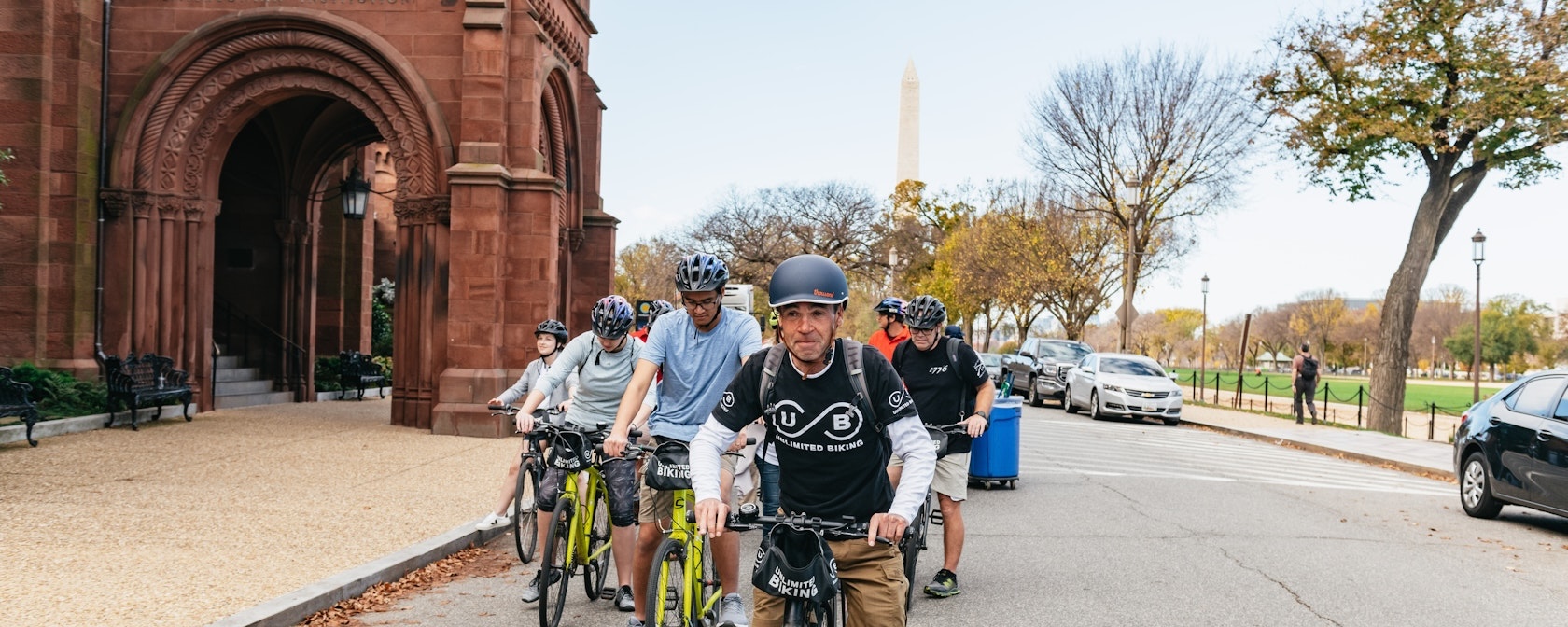 A guide leads a biking tour along the National Mall with the Smithsonian Castle and the Washington Monument in the background. 