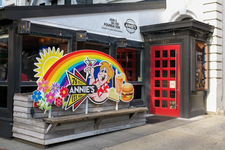 A colorful sign outside of a restaurant with a woman holding a burger and a large rainbow. 