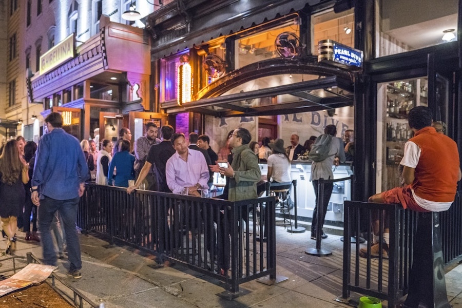 A lively crowd gathers outside Pearl Dive Oyster Palace on 14th Street at night, with open-air bar seating and vibrant lighting.