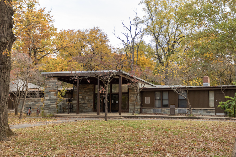 A low, stone and wood nature center building surrounded by colorful fall foliage in a quiet forest setting.