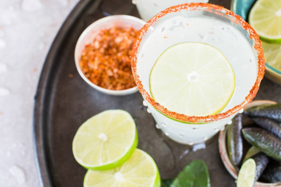 A gin rickey garnished with a lime wheel is served with chili lime salt, surrounded by fresh citrus.