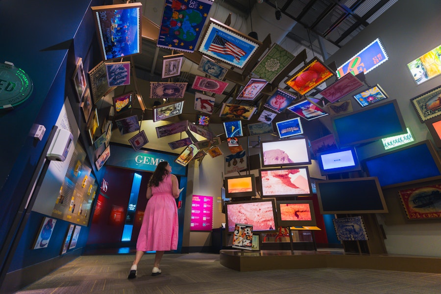 A visitor looks up at a colorful ceiling display of stamps and screens in the Postal Museum's stamp gallery.