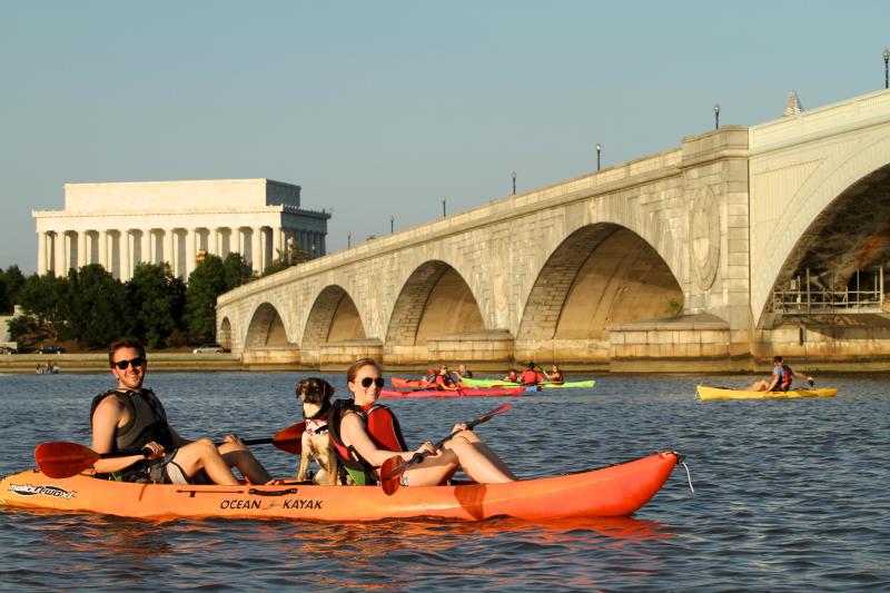 People and a dog enjoy kayaking on the Potomac River near the Lincoln Memorial and Arlington Memorial Bridge.