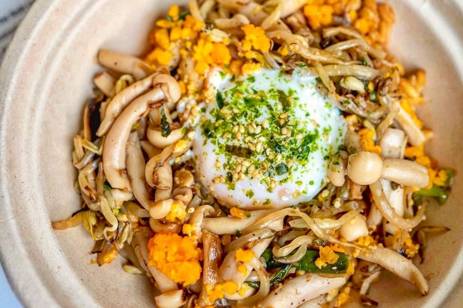A colorful bowl of sautéed mushrooms, shredded vegetables, orange crumbles and a soft-boiled egg topped with herbs and sesame seeds.
