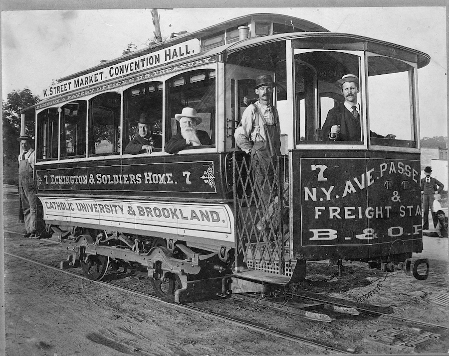 Black-and-white photo of a Washington, DC, streetcar with conductors and passengers, marked for routes to K Street Market, Convention Hall and Brookland. 