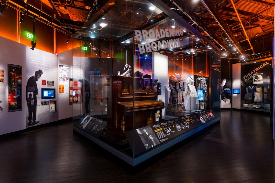 Display case with costumes and a piano in the “Broadening Broadway” exhibit at the National Museum of African American History and Culture.