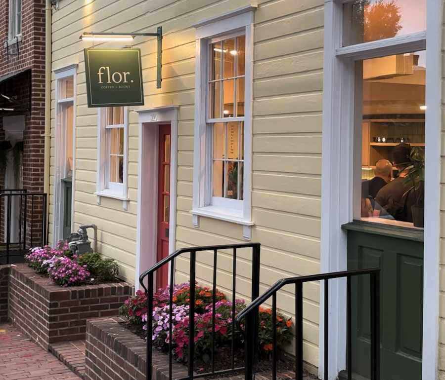 The exterior of Flor Coffee + Books, a quaint home painted yellow with inviting flowers and a red door. 