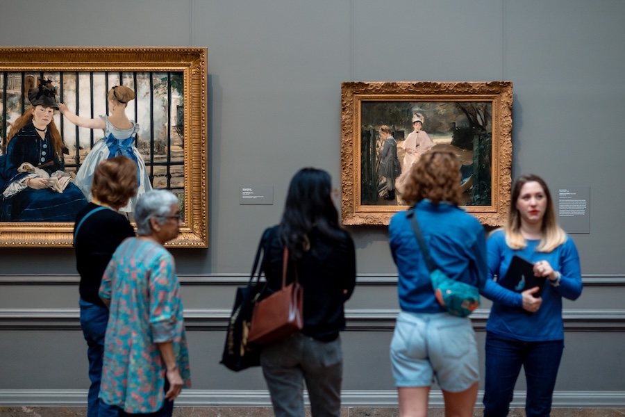 A group stands with a tour guide in front of a series of French paintings in the National Gallery of Art in Washington, DC. 