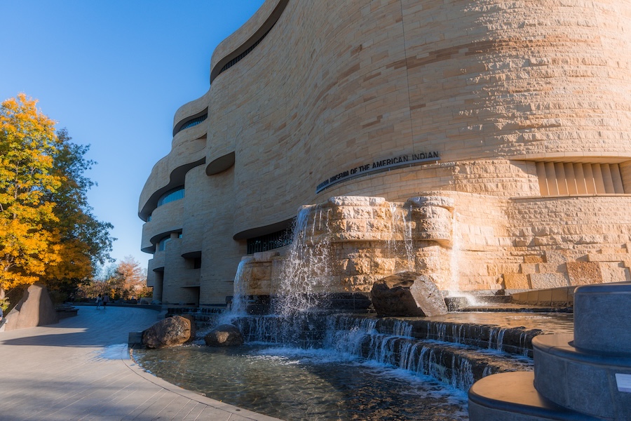 A cascading waterfall flows beside the curved stone exterior of the National Museum of the American Indian.