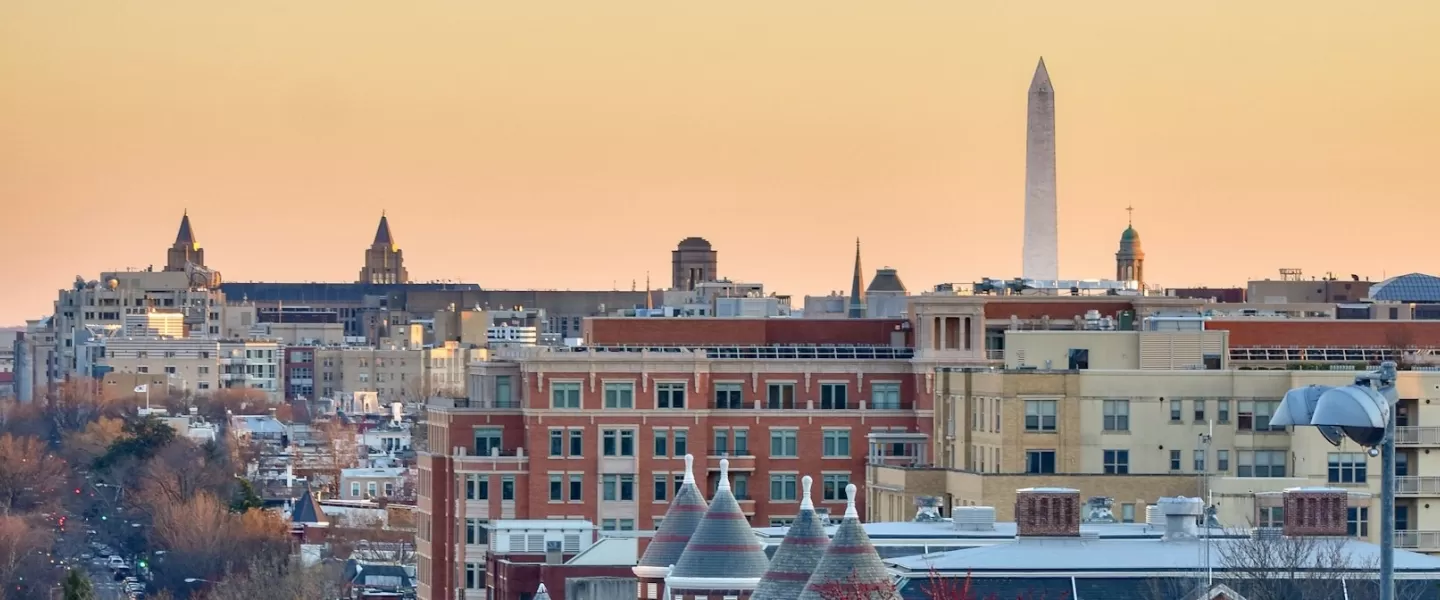 A photo of the DC skyline at sunset with the Washington Monument just beyond the historic buildings below. 