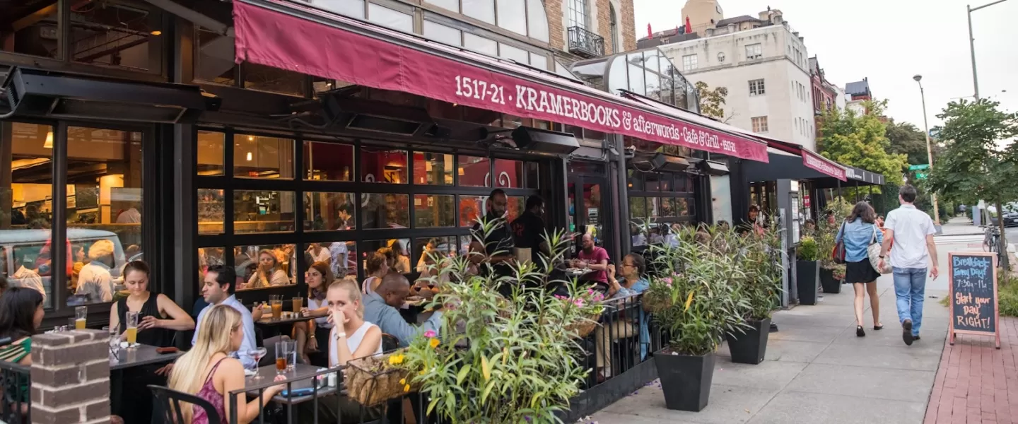 Diners enjoy outdoor seating at Kramerbooks & Afterwords Café in Dupont Circle as pedestrians stroll past the bustling sidewalk café.