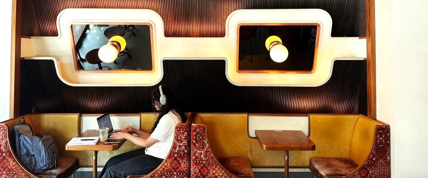 A person wearing headphones works at a booth in a stylish café with retro lighting and mid-century modern decor.