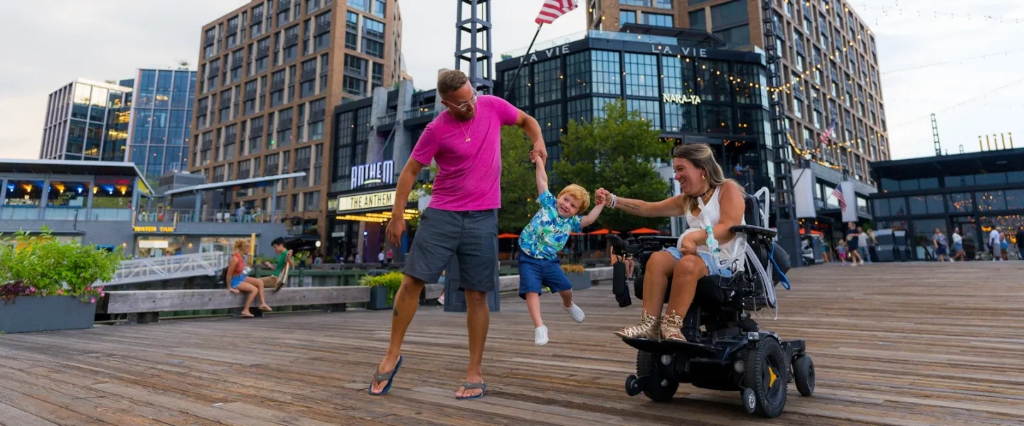 Parents hold their child's hands and swing him in the air as they enjoy a day on the Wharf. 