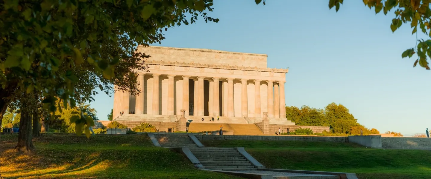 The Lincoln Memorial at sunset framed by trees with golden light on the monument’s columns.