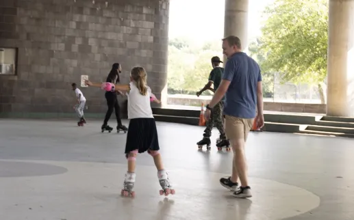 A father walks beside his daughter while she rollerblades. 