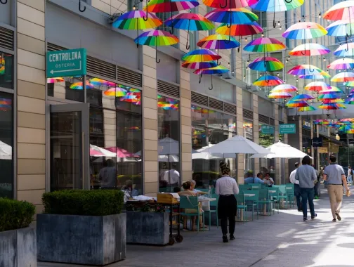 People walk and dine beneath a canopy of colorful rainbow umbrellas outside Centrolina at CityCenterDC.