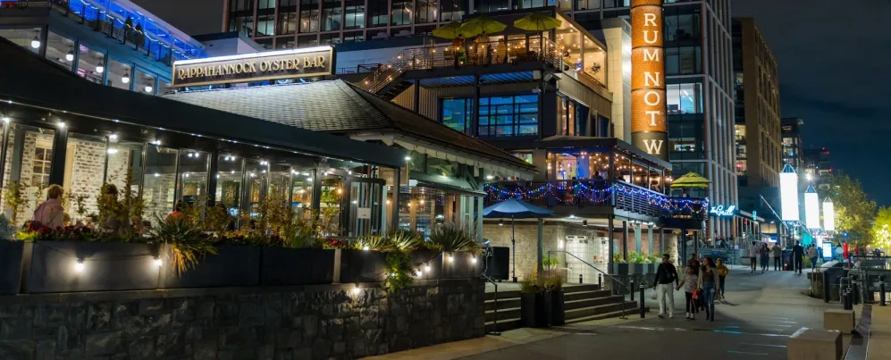 Businesses are lit up and busy at night along The Wharf in DC. 
